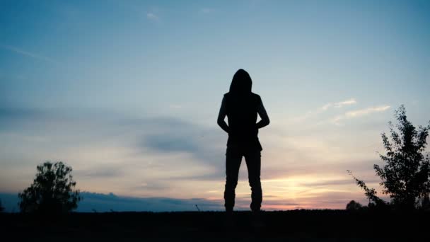 Una persona en una capucha está sola durante el atardecer en un campo contra un hermoso cielo — Vídeos de Stock