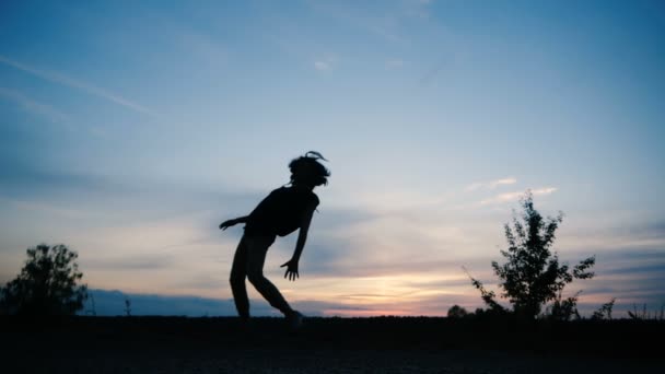Silhueta de um menino com cabelos longos que está dançando hip hop ao pôr do sol, câmera lenta — Vídeo de Stock