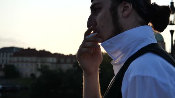 4k-chlapík z brunetu klidně kouří cigaretu na mostě Prahy, pomalý pohyb — Stock video