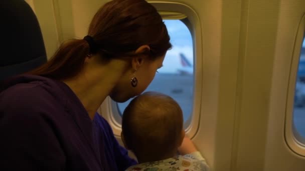 Дівчина і її маленький син дивиться у вікно літака в повільному русі — стокове відео