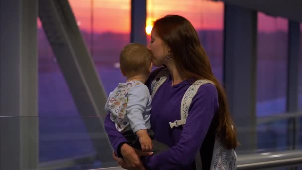 Ładna dziewczyna trzyma na rękach małego syna na lotnisku w pobliżu okna, powolny ruch — Wideo stockowe