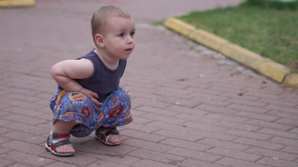 Маленький блондин приседает на дороге и смотрит вверх, замедленное движение — стоковое видео