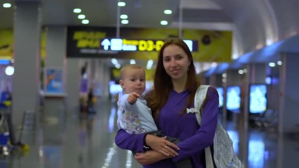 Sonriente madre lleva a un hermoso bebé alrededor del aeropuerto en cámara lenta — Vídeo de stock