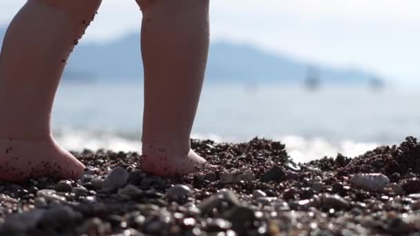 Cerca de las pequeñas piernas de bebé de pie en la arena junto al mar en cámara lenta — Vídeo de stock