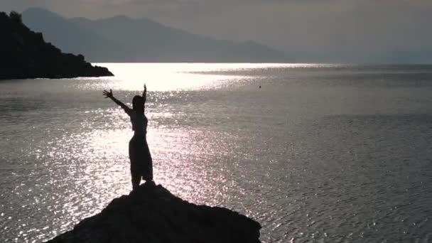 Hermosa chica en una piedra sobre el mar mostrando un gesto de victoria en cámara lenta — Vídeos de Stock