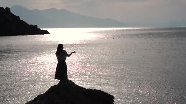 Romanrtic kadın gün doğumunda yavaş çekimde deniz tarafından bir kaya üzerinde dans — Stok video
