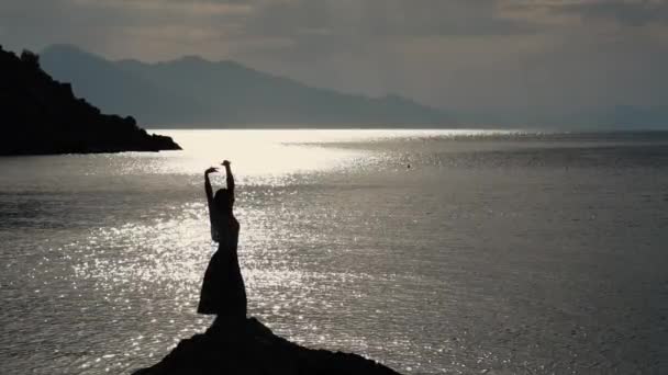 Gün batımında yavaş çekimde denizin yanında bir kayanın üzerinde dans eden güzel kadın. — Stok video