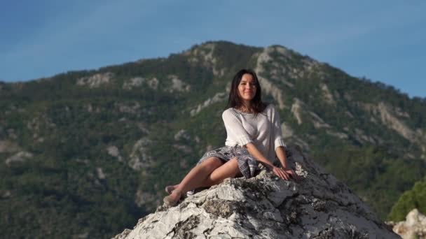 Attraktive brünette Frau sitzt an einem sonnigen Tag in Zeitlupe auf einem Felsen — Stockvideo