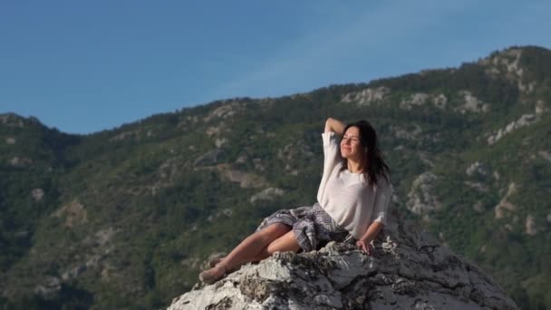 Красивая брюнетка молодая женщина сидит на скале в замедленной съемке в солнечный день — стоковое видео
