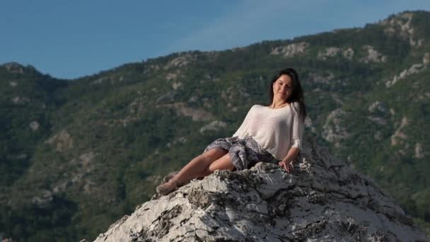 Gyönyörű fiatal nő modell ül a sziklán egy napsütéses napon, lassú mozgás — Stock videók