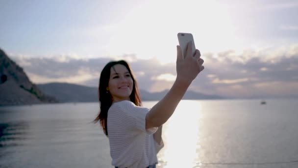 Bonita morena joven mujer hace fotos selfies contra el mar al amanecer en cámara lenta — Vídeos de Stock