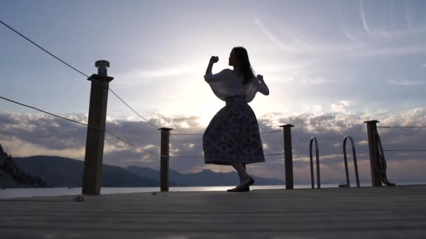 Брюнетка в пишній спідниці танцює біля моря на сході сонця, повільний рух — стокове відео
