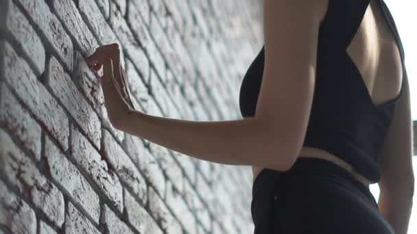 Арти блондинка идет с пальцем на кирпичной стене и похлопывает его в студии в slo-mo — стоковое видео