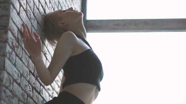 Arty meisje zittend op een bakstenen muur als een sculptuur en het zetten van de handen naar beneden in een studio in slo-mo — Stockvideo