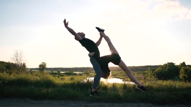 Arty blond kille står och håller sin tjej gör en front Split mellan benen vid en sjö i slo-mo — Stockvideo