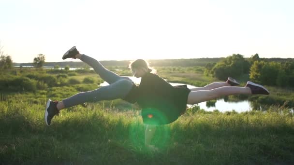 Homem louro forte faz um suporte com uma menina mantendo as pernas opostas ao pôr do sol em slo-mo — Vídeo de Stock