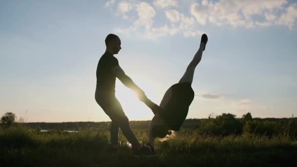 Artistic blond man keeps his girl doing a straddle split standing on her hands at lake in slo-mo — Stock Video