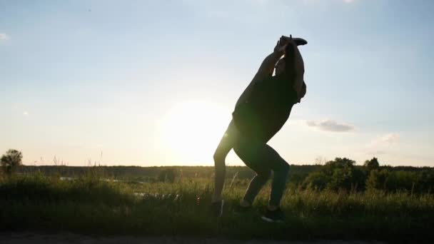 Arty homem forte mantém sua menina fazendo uma divisão dianteira em suas costas ao pôr do sol em slo-mo — Vídeo de Stock