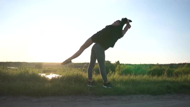 Genç adam bir ön bölünmüş yapıyor onun kız tutar ve onu slo-mo gün batımında ayağa yardımcı olur — Stok video