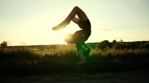 Chica flexible haciendo un soporte de mano con las piernas dobladas hacia atrás en un lago al atardecer en slo-mo — Vídeo de stock