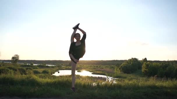 Lustiges Mädchen, das bei Sonnenuntergang in Slo-mo an einem See steht und einen Straddle Oversplit macht — Stockvideo