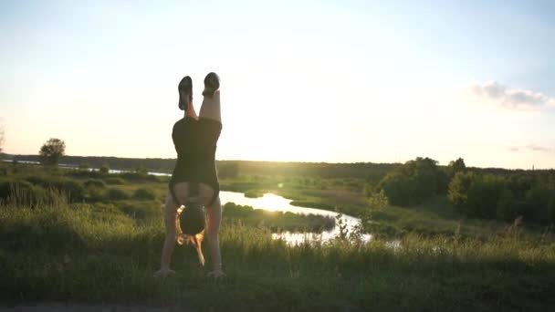 Atletik kız bir kartal-handstand yapıyor ve slo-mo gün batımında bir gölet ayakta — Stok video