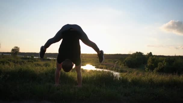Silny młody człowiek robi pochyleniem dodatnim Handstand na jeziorze o wspaniałym zachodzie słońca w SLO-mo — Wideo stockowe
