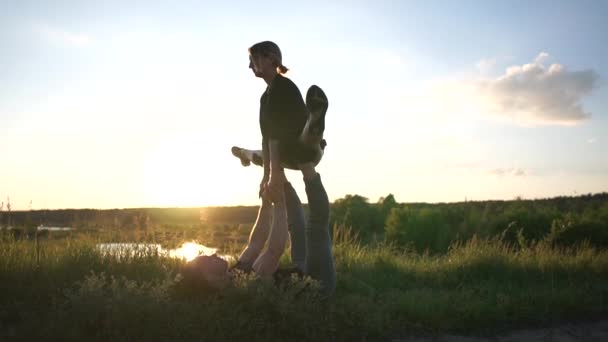 L'homme sportif ment et continue sa fille à faire une fente de cheval au lac au coucher du soleil. — Video