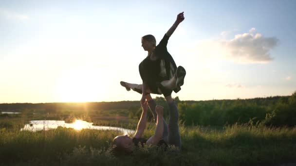 Homem resistente mente e mantém sua menina fazendo uma divisão na lagoa ao pôr do sol n slo-mo — Vídeo de Stock