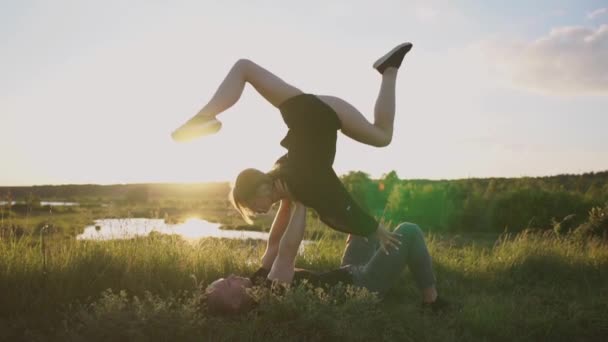 Robusto uomo si trova e mantiene la sua ragazza facendo una spaccatura davanti al lago al tramonto n slo-mo — Video Stock