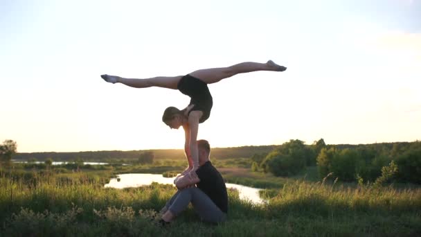 Uomo sportivo si siede e tiene la sua ragazza in ginocchio facendo una spaccatura davanti al tramonto in slo-mo — Video Stock