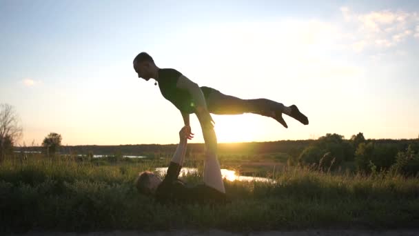 Chica fuerte miente y mantiene a su chico en sus pies haciendo una figura de gorrión al atardecer en slo-mo — Vídeo de stock