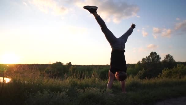 Hulk homem faz um suporte de mão com um straddle dividir pernas girando direito ao pôr do sol em slo-mo — Vídeo de Stock