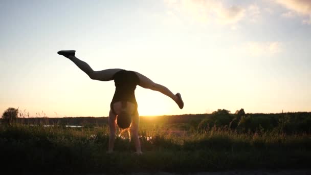 Ισχυρό κορίτσι κάνει ένα χέρι με ένα μπροστινό χώρισμα και μια μπροστινή διάσπαση στη λίμνη κατά το ηλιοβασίλεμα σε αργή-mo — Αρχείο Βίντεο