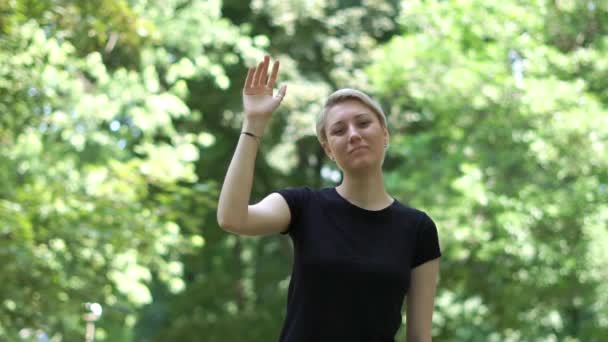 Teleurgesteld jonge blonde vrouw zwaaiende afscheid in een groen park in slo-mo — Stockvideo