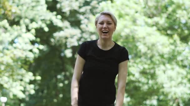 Mujer rubia feliz riendo y levantando las manos en un parque en slo-mo — Vídeo de stock