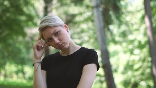 Prachtige blonde vrouw staande en aanraken van haar tempel in een groen bos in slo-mo — Stockvideo