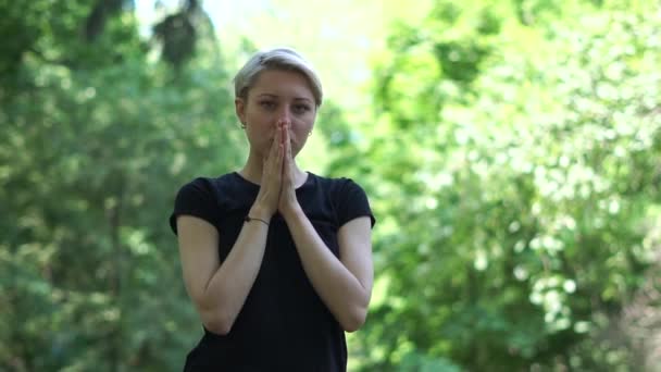 Елегантна жінка стоїть і тримає руки в молитовному положенні в лісі в шлю-мо — стокове відео