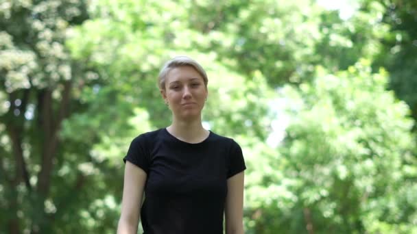 Уверенная блондинка, показывающая ОК жест и улыбки в зеленом парке в сло-мо — стоковое видео