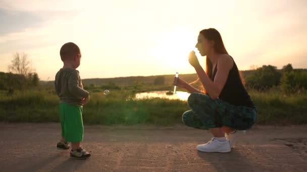 Komik anne oturma ve slo-mo gün batımında çocuğu için sabun kabarcıkları yapma — Stok video