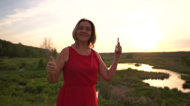 Šťastná žena tančí se svým smartphone v drsným rybníku při západu slunce v slo-mo — Stock video