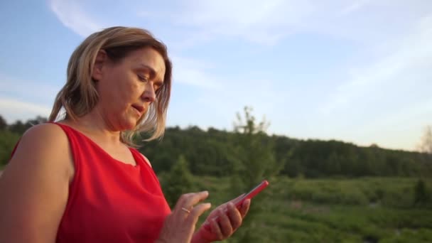快乐的女人拨号和短信在她的智能手机在小池塘在日落在slo-mo — 图库视频影像