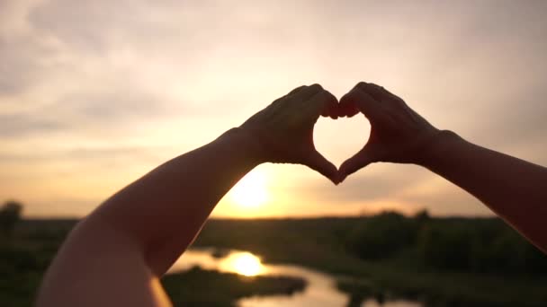 Női kezek csinálás egy szív jel-on picike nád tó-on szép naplemente-ban slo-Mo