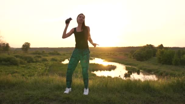 Stylová mladá žena tančící s lahví vína u jezera při západu slunce v slo-mo — Stock video