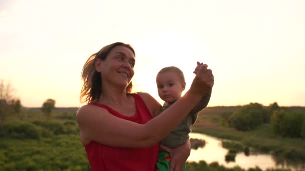 Mulher feliz dançando com uma criança no pequeno lago ao pôr do sol em slo-mo — Vídeo de Stock