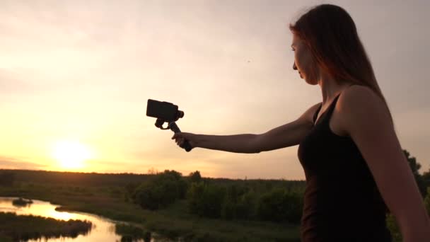 Mujer joven delgada disparando paisaje con un teléfono inteligente al atardecer en slo-mo — Vídeo de stock