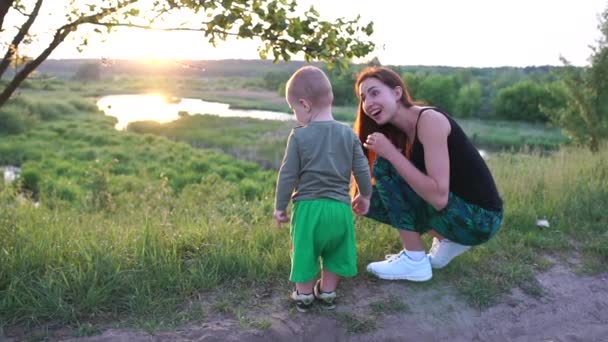 Счастливая мать сидит и разговаривает со своим ребенком на маленьком озере на закате в сло-мо — стоковое видео