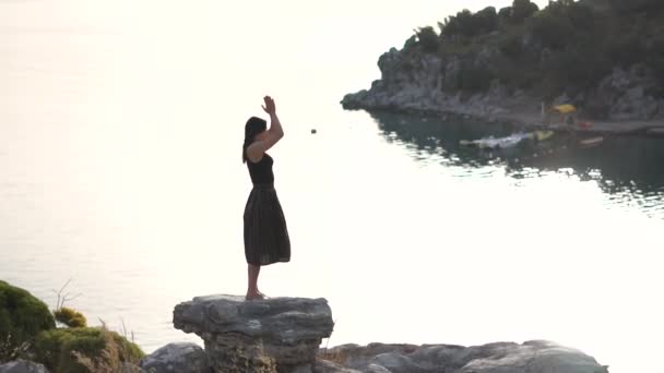 Молодая девушка молится и благодарит Бога, стоя на скале у моря, медленное движение — стоковое видео