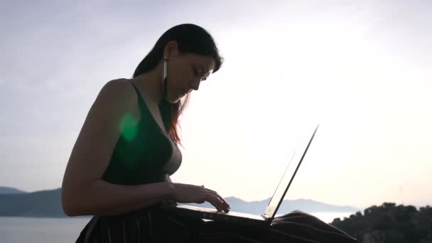 Uma estudante trabalha em um laptop em uma rocha acima do mar, em câmera lenta — Vídeo de Stock