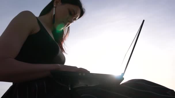 Brunetka pracuje v notebooku, který sedí bosé vysoko na skále nad mořem — Stock video
